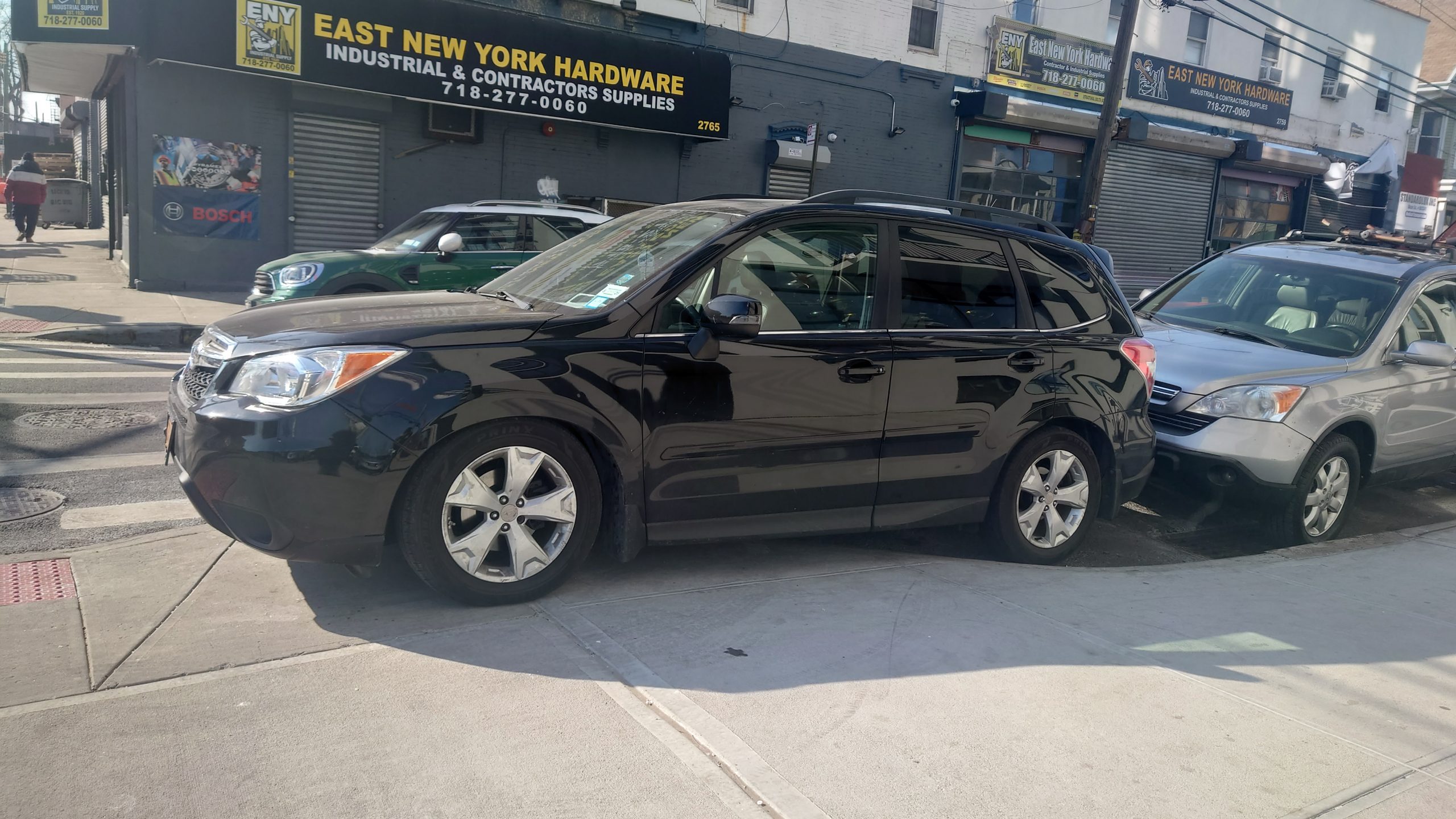 black car half parked on the sidewalk and half parked in the street