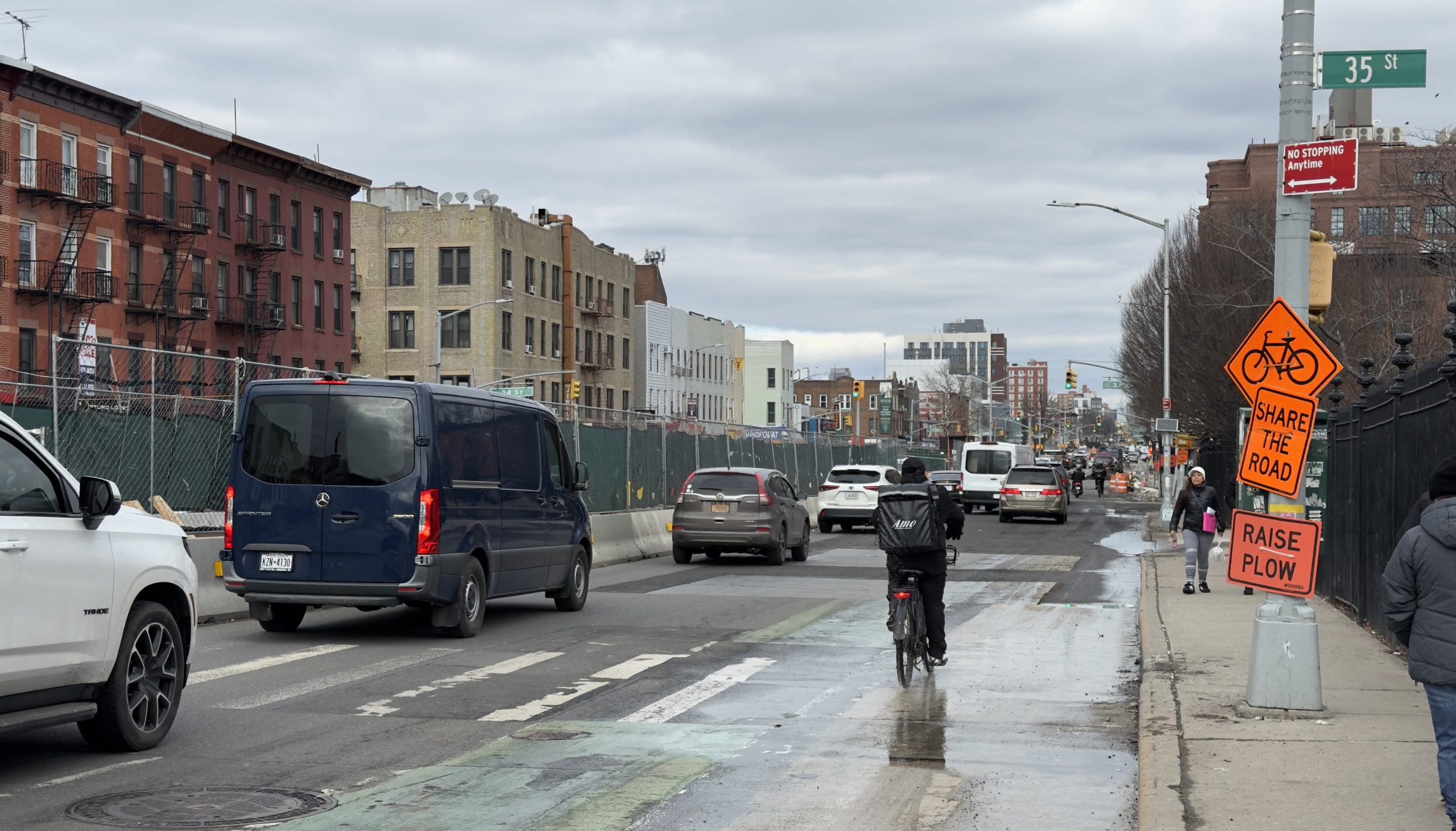 A person riding a bicycle navigates a signed work zone on 4th Avenue, sharing the lane with motor vehicles amid construction debris and metal roadway plates.